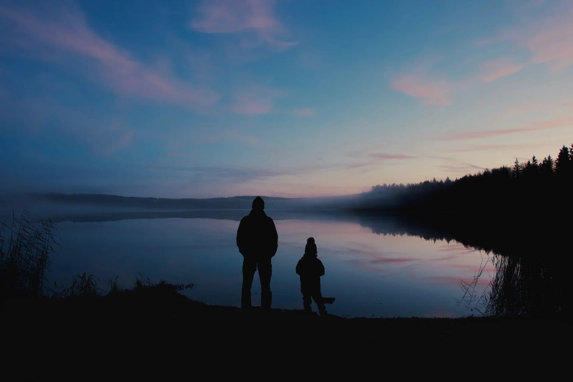 Two people looking across a quiet lake at dusk